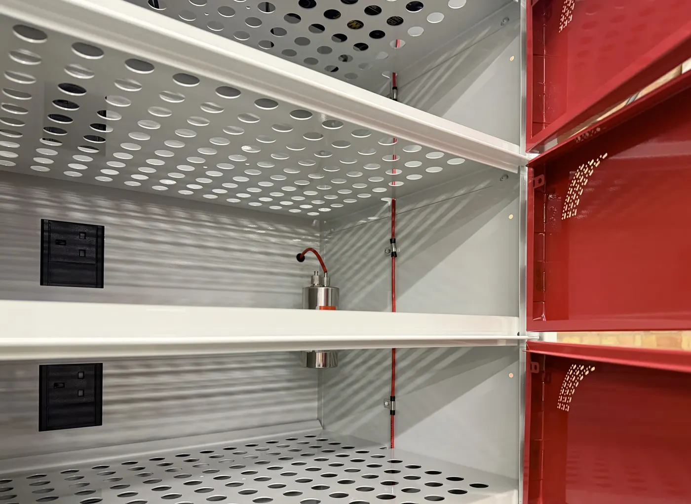 Inside a locker compartment: perforated shelves and 3-pin socket