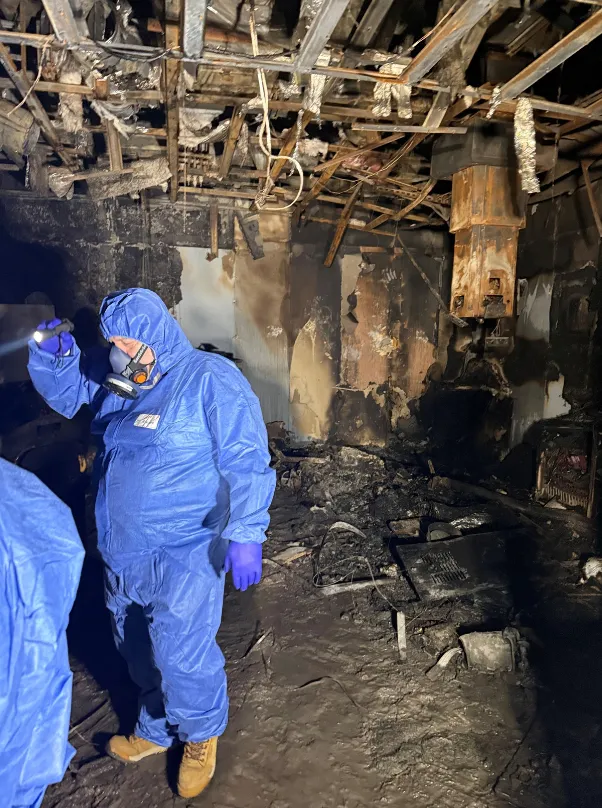 Investigator in protective suit and respirator inspecting a fire-gutted hospital area